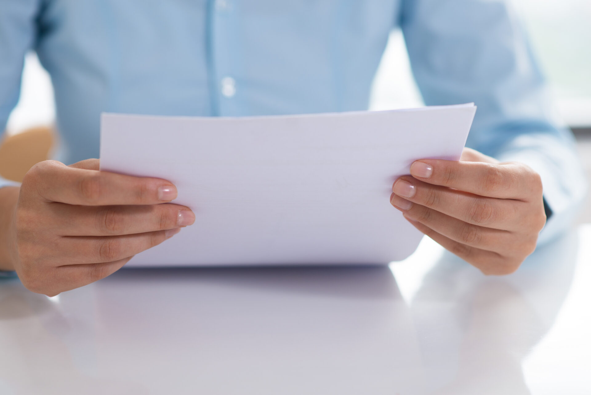 Energieausweis-Dokument auf weißem Papier in den Händen, blaues Hemd, ruhige Nahaufnahme mit unscharfem Hintergrund und professioneller Unterlagen-Optik