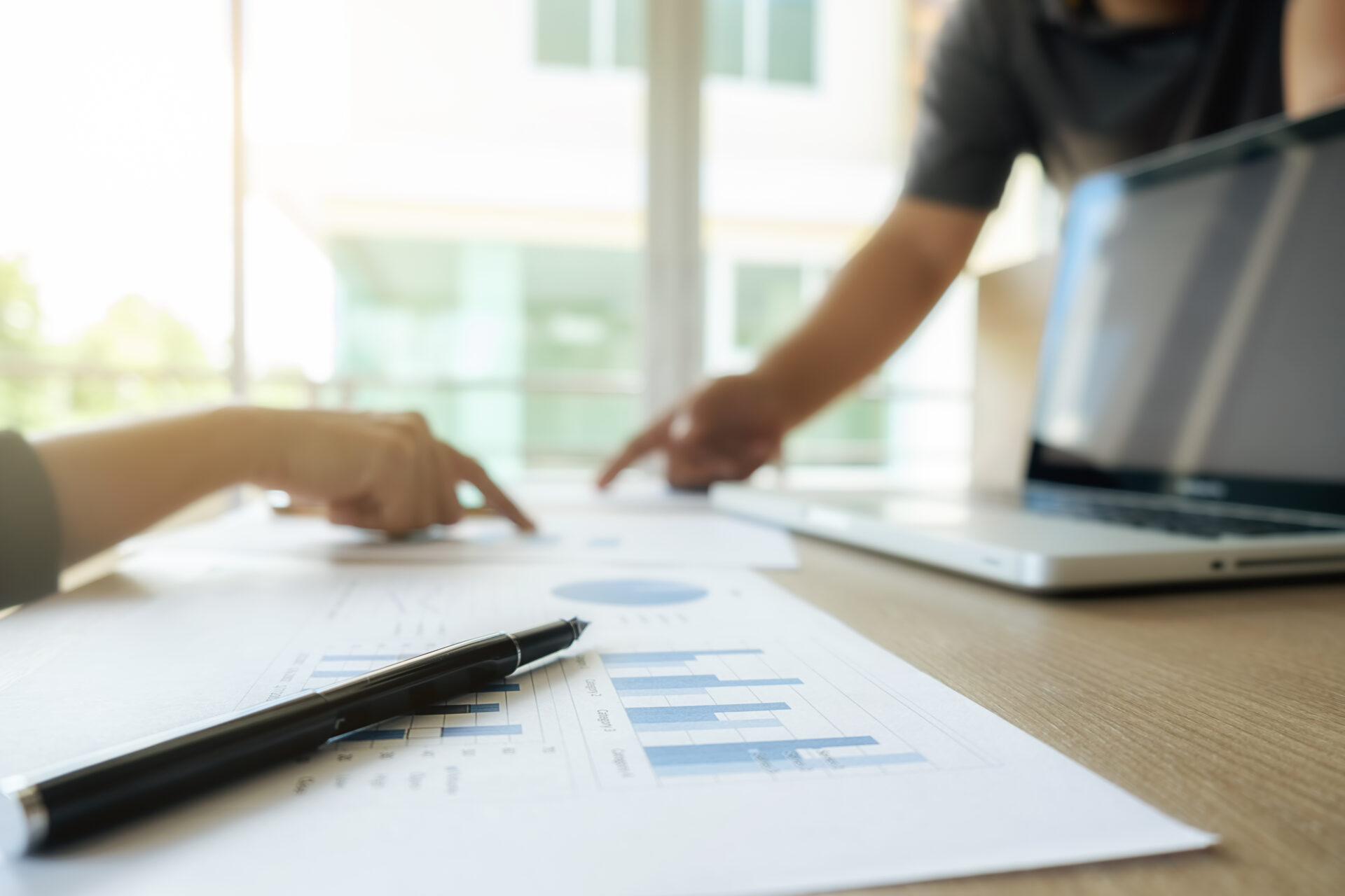 Wertermittlung bei der Immobilien Beratung & Vermittlung: Hände besprechen Bauunterlagen mit Stift und Tablet-Laptop, übersichtliche Pläne und Tabellen